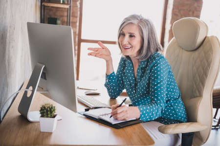 Profile photo of positive old lady talk laptop write sit wear blue shirt work at home alone