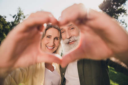Photo of sweet senior white hair couple show heart wear casual shirts outdoors walk in parkの写真素材