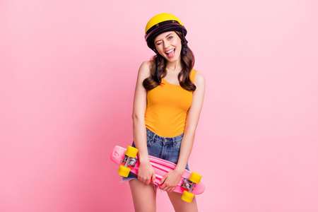 Photo of cute millennial curly hairdo lady blink eye hold skate wear orange top helmet shirts isolated on pink color backgroundの写真素材