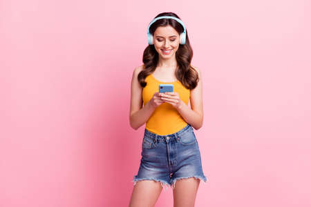 Photo of sweet shiny young lady dressed yellow tank-top typing modern device listening songs isolated pink color backgroundの写真素材