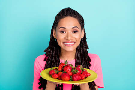 Photo of cheerful adorable girl hold dish strawberry wear pink t-shirt isolated on blue color backgroundの写真素材