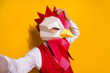 Photo of funky weird guy hold camera take festive selfie wear cock mask red suit isolated yellow color backgroundの写真素材