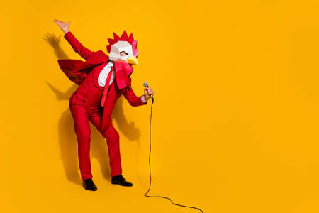 Photo of crazy anonymous guy hold mic sing song have clubbing fun wear rooster mask red tux isolated yellow color backgroundの写真素材
