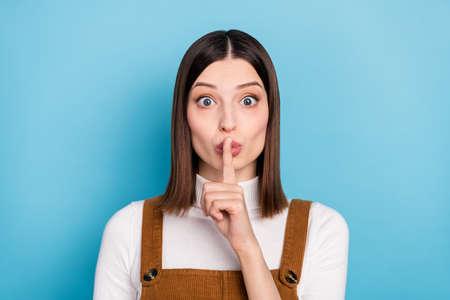 Photo of young pretty girl finger cover mouth keep secret confidential information isolated over blue color backgroundの写真素材