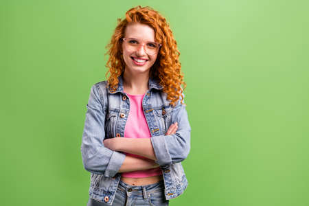 Photo of confident shiny young woman wear jeans outfit spectacles arms crossed empty space smiling isolated green color backgroundの写真素材