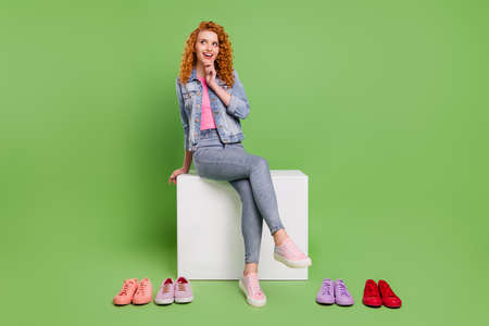 Full size photo of young girl happy positive smile think choose buy sneakers look empty space isolated over green color backgroundの写真素材