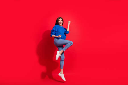 Full length photo of cheerful young charming woman jump up winner fists isolated on red color backgroundの写真素材