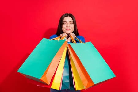 Photo of cheerful happy cute nice young woman enjoy shopping hold bags isolated on red color backgroundの写真素材