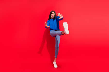 Full length photo of attractive young nice funny woman raise leg hands dance isolated on red color backgroundの写真素材