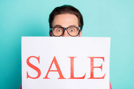 Photo of funny impressed young guy dressed pink shirt spectacles sale poster cover face isolated turquoise color backgroundの写真素材