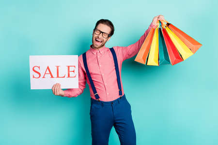 Photo of young excited man happy smile hold banner sale shopaholic bags isolated over turquoise color backgroundの写真素材