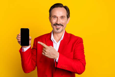 Photo of elegant luxury well-dressed man advertising smartphone touch screen isolated on yellow color backgroundの写真素材