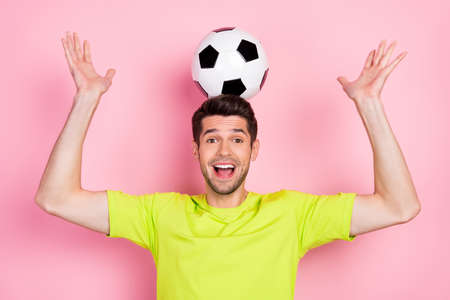 Portrait of attractive playful cheerful guy holding soccer ball on head having fun isolated over...