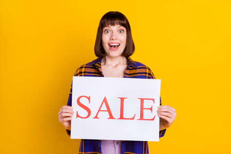 Portrait of attractive cheerful amazed girl holding in hands sale board isolated over bright yellow color backgroundの写真素材