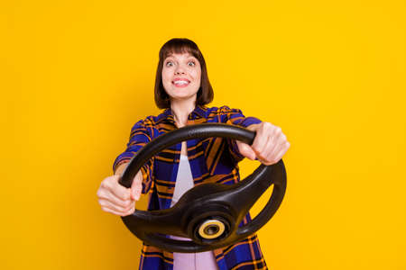Portrait of attractive girlish cheerful girl holding steering wheel practicing isolated over bright yellow color backgroundの写真素材