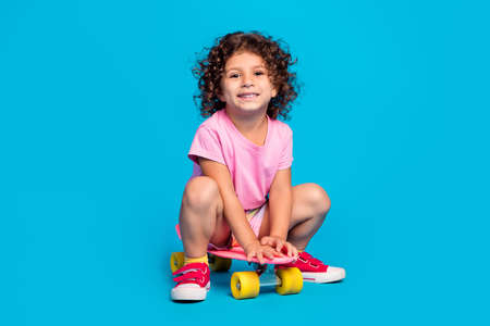 Portrait of attractive cheerful wavy-haired girl riding skate pastime isolated over bright blue...