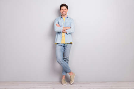 Photo of pretty confident young guy wear jeans shirt arms crossed empty space isolated concrete grey wall backgroundの写真素材
