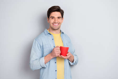 Photo of cheerful attractive guy dressed denim shirt enjoying hot coffee isolated grey color...