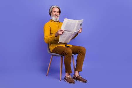 Full length body size view of attractive cheerful gray-haired man reading page isolated over bright...