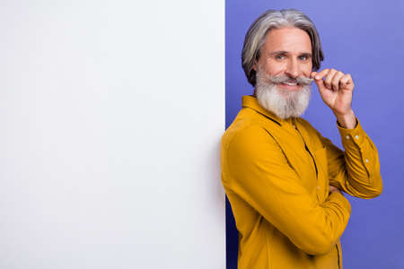 Portrait of attractive cheery gray-haired man copy space touching moustache isolated over bright violet purple color backgroundの写真素材