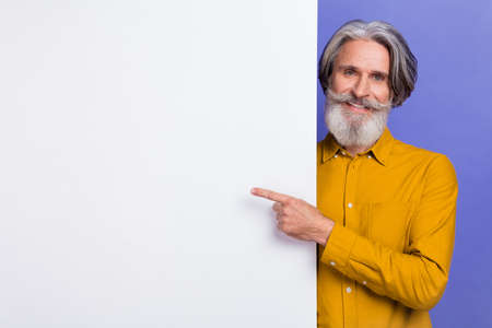 Portrait of attractive cheery gray-haired man demonstrating copy place space ad isolated over bright violet purple color backgroundの写真素材