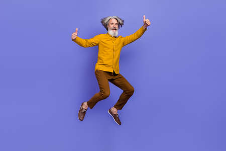 Full length body size view of attractive cheery gray-haired man jumping showing thumbup isolated over bright violet purple color backgroundの写真素材