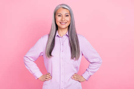 Portrait of attractive cheerful successful gray-haired woman hands on hips isolated over pink pastel color backgroundの写真素材