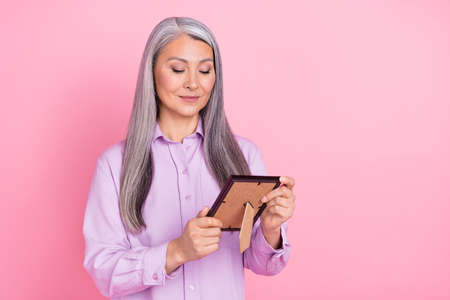 Portrait of attractive cheery dreamy gray-haired woman looking at photo picture isolated over pink pastel color backgroundの写真素材