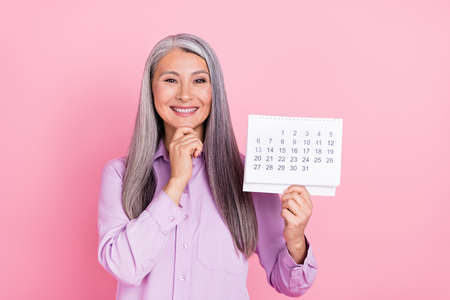 Portrait of attractive glad cheerful gray-haired woman holding calendar new year isolated over pink pastel color backgroundの写真素材