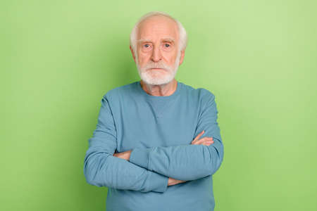 Photo of strict aged beard man crossed palms wear blue pullover isolated on green color backgroundの写真素材
