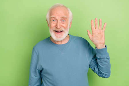 Photo of impressed aged beard man wave wear blue sweater isolated on green color backgroundの写真素材