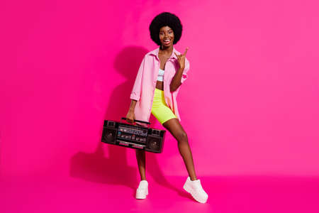 Photo of sweet rude dark skin woman dressed crop top showing har rock sign listening boombox isolated pink color backgroundの写真素材