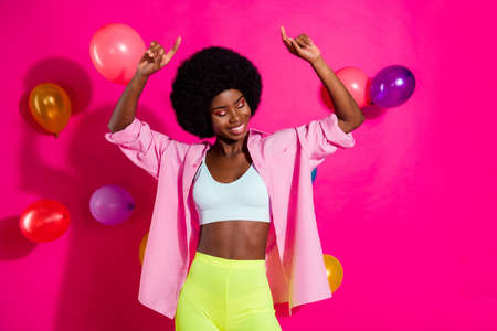 Photo of shiny charming dark skin woman dressed crop top dancing flying balloons pointing fingers isolated pink color backgroundの写真素材