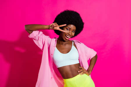 Photo of adorable cute dark skin lady wear casual shirt showing v-sign dancing smiling isolated pink color backgroundの写真素材