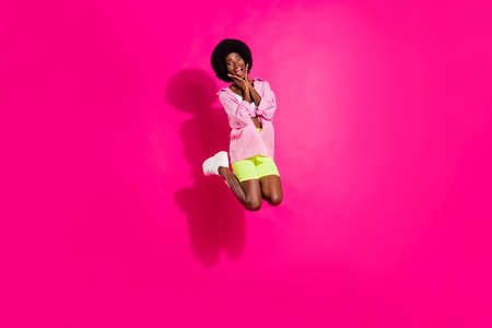 Full size photo of young excited african girl happy positive smile amazed surprised jump isolated over pink color backgroundの写真素材