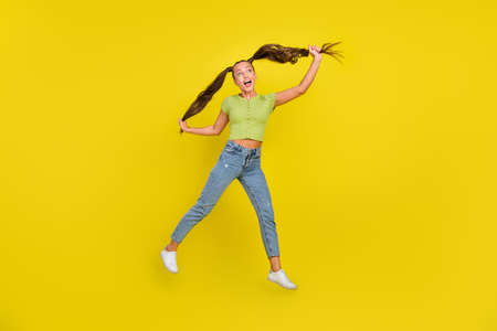 Full length photo of impressed millennial brunette lady jump look empty space wear jeans t-shirt shoes isolated on yellow backgroundの写真素材