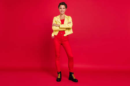 Photo of charming shiny young woman dressed leather jacket walking arms crossed smiling isolated red color backgroundの写真素材