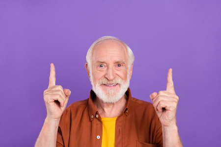 Photo of optimistic old man index empty space wearing brown shirt isolated over purple color backgroundの写真素材