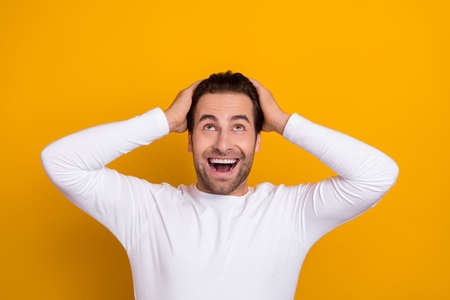Photo of positive astonished man arms on head look interested above empty space isolated on yellow color backgroundの写真素材
