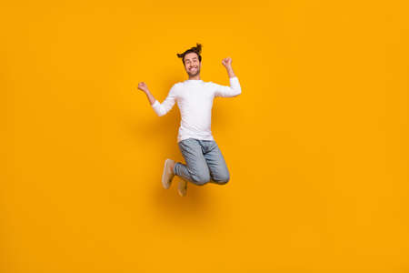 Full length photo of cool brunet young guy jump hands fists wear shirt jeans footwear isolated on yellow backgroundの写真素材