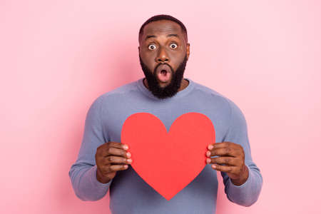 Photo of shocked speechless guy hold heart symbol open mouth wear grey shirt isolated pink color backgroundの写真素材