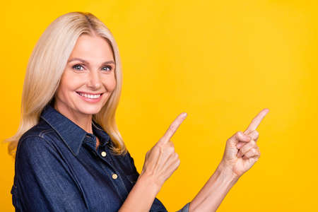 Photo of cute shiny lady pensioner dressed denim outfit pointing empty space isolated yellow color...