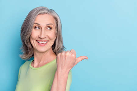 Photo of charming happy nice old woman look point finger empty space choose isolated on blue color backgroundの写真素材