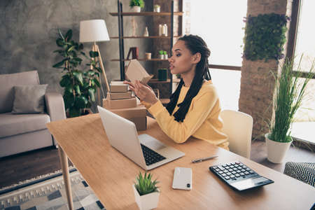 Photo of busy confident young lady wear yellow pullover working modern device holding boxes indoors...