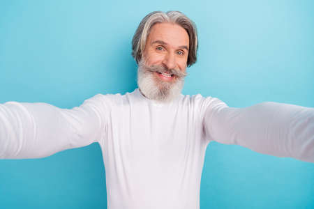 Self-portrait of attractive cheerful grey-haired man good mood isolated over bright blue color...