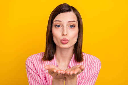 Photo of adorable coquettish lady hands send air kiss you look camera isolated on yellow color backgroundの写真素材