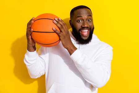 Photo of impressed young beard man play basketball wear white hoodie isolated on yellow color backgroundの写真素材