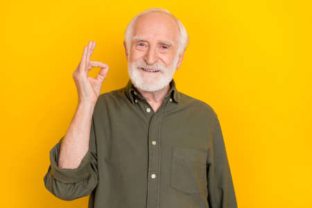 Portrait of positive cheerful aged man fingers show okey symbol toothy smile isolated on yellow color backgroundの写真素材