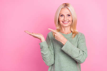 Photo of charming cute lady pensioner dressed green pullover holding arm empty space isolated pink...