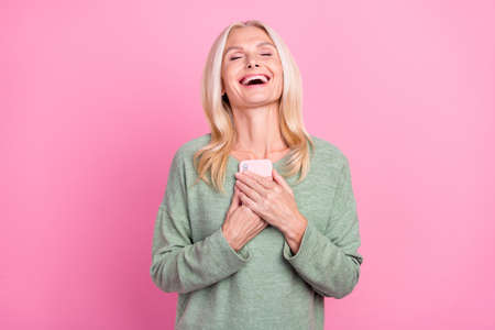 Photo of shiny funny retired woman wear green sweater read modern gadget laughing isolated pink...